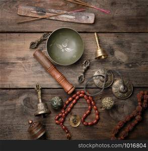 Copper singing bowl, prayer beads, prayer drum and other Tibetan religious objects for meditation and alternative medicine on a brown wooden background