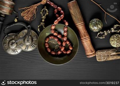 Copper singing bowl, prayer beads, prayer drum, stone balls and other Tibetan religious objects for meditation and alternative medicine on a black wooden background, top view