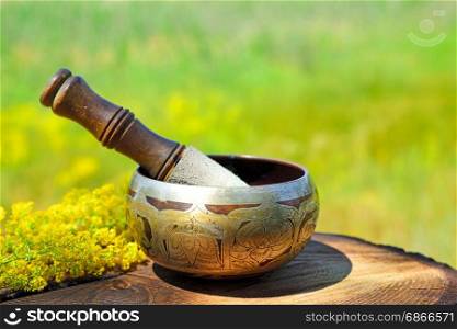 Copper singing bowl with a stick on a wooden table, blurred background of nature