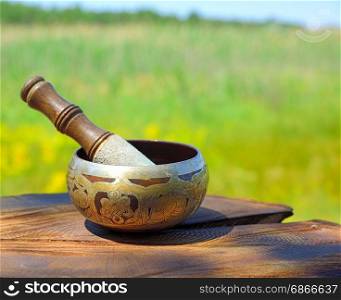 Copper Tibetan singing bowl on a brown wooden background, blurred background