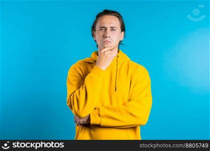 Copy space. Thinking man looking up and around on blue background. Worried contemplative face expressions. Handsome male model in yellow wear. High quality photo. Copy space. Thinking man looking up and around on blue background. Worried contemplative face expressions. Handsome male model in yellow wear
