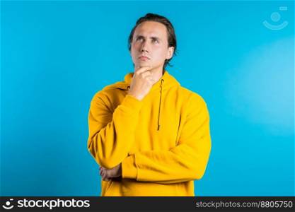 Copy space. Thinking man looking up and around on blue background. Worried contemplative face expressions. Handsome male model in yellow wear. High quality photo. Copy space. Thinking man looking up and around on blue background. Worried contemplative face expressions. Handsome male model in yellow wear