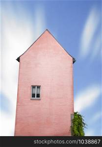 Coral colored building tower with one window against a blue sky. German old house, tall, with just one window, isolated. Minimal surreal architecture.