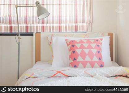 Coral pink triangle pattern pillow setting on bed with foldable reading lamp next to bed