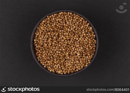 Coriander seeds in small bowl on dark background