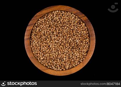 Coriander seeds in small wooden bowl on dark background