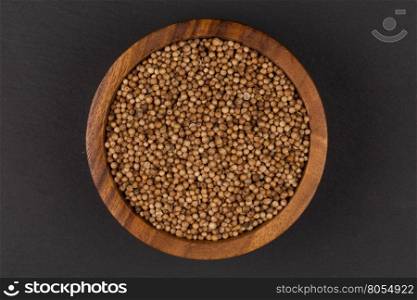 Coriander seeds in small wooden bowl on dark background