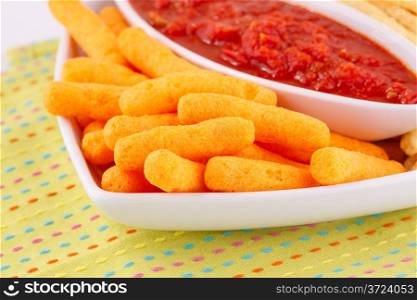 Corn chips and red sauce on colorful tablecloth.