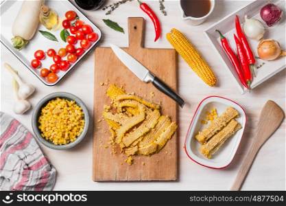 Corn cooking preparation with cutting board, knife and ingredients on white wooden kitchen table background, top view
