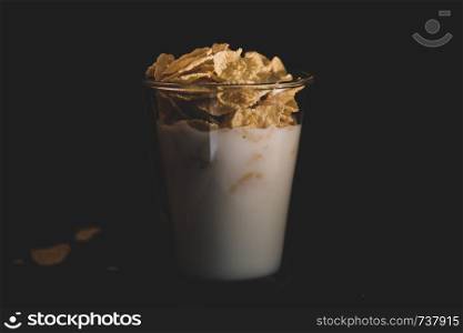Corn flakes with milk in glass cup isolated on black background. Corn flakes with milk in glass cup isolated on black