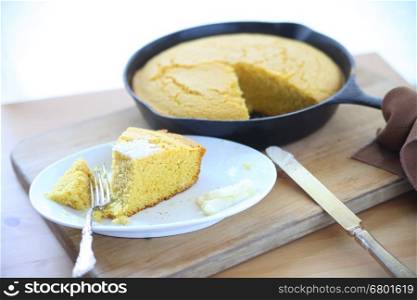 Cornbread baked in a cast iron skillet with a wedge on a small dish with butter