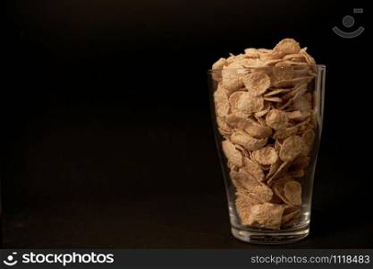 cornflakes in a transparent glass against a black background with place for text. cornflakes in a transparent glass against a black background