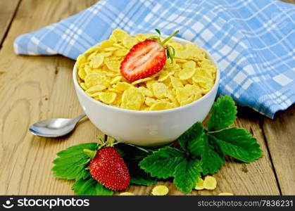 Cornflakes in a white bowl with half a strawberry, leaves and strawberries, napkin on wooden board