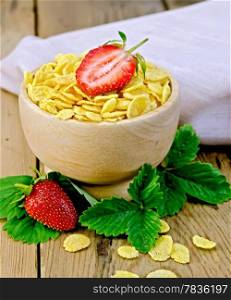 Cornflakes in wooden bowl, strawberry leaves and berries, a napkin on a wooden boards background