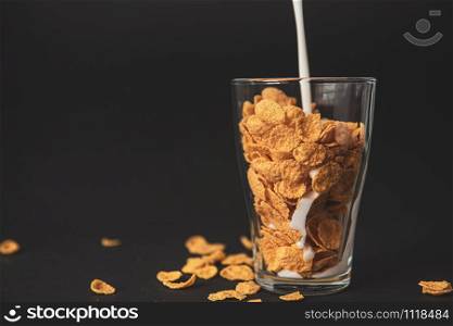 cornflakes with milk in a transparent glass against a black background with place for text. cornflakes with milk in a transparent glass against a black background