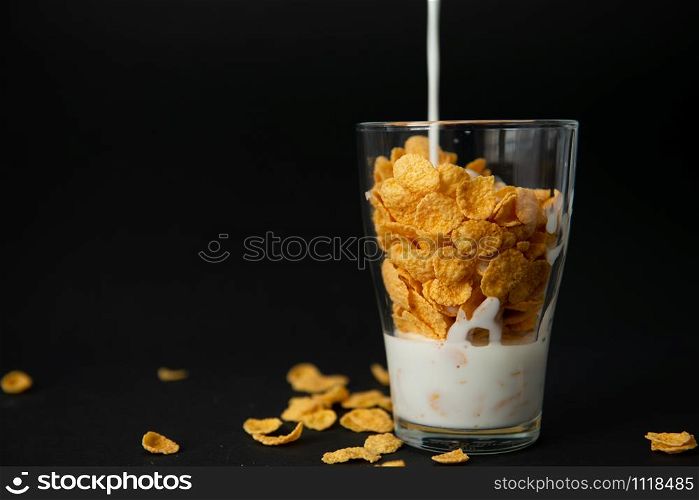 cornflakes with milk in a transparent glass against a black background with place for text. cornflakes in a transparent glass against a black background