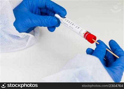 Coronavirus COVID-19 testing kit,swab collection equipment,sterile vacutainer with swabbing stick,closeup of hands in blue protective gloves holding the test tube,rt-PCR s&le specimen testing