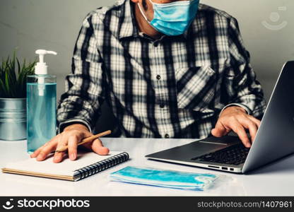 Coronavirus disease or COVID-19 protection concept - Young man work in office room at home with protective and cleaning equipment to protect against corona virus while using laptop computer at desk.