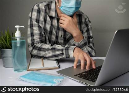 Coronavirus disease or COVID-19 protection concept - Young man work in office room at home with protective and cleaning equipment to protect against corona virus while using laptop computer at desk.