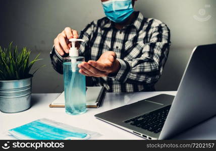 Coronavirus disease or COVID-19 protection concept - Young man work in office room at home with protective and cleaning equipment to protect against corona virus while using laptop computer at desk.