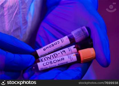 Coronavirus, Doctor holding positive covid 19 virus Blood Sample test tube. Wearing biohazard epidemic Protective mask, suit and glows neon light background