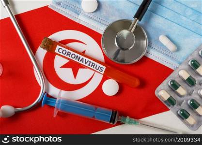 Coronavirus, nCoV concept. Top view of a protective breathing mask, stethoscope, syringe, pills on the flag of Tunisia. A new outbreak of the Chinese coronavirus. Coronavirus, nCoV concept. Top view of a protective breathing mask, stethoscope, syringe, pills on the flag of Tunisia.