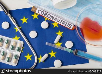 Coronavirus, nCoV concept. Top view protective breathing mask, stethoscope, syringe, pills on the flag of Europe. A new outbreak of the Chinese coronavirus. Coronavirus, nCoV concept. Top view protective breathing mask, stethoscope, syringe, pills on the flag of Europe.