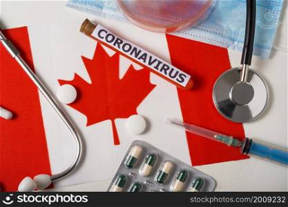 Coronavirus, nCoV concept. Top view protective breathing mask, stethoscope, syringe, pills on the flag of Canada. A new outbreak of the Chinese coronavirus. Coronavirus, nCoV concept. Top view protective breathing mask, stethoscope, syringe, pills on the flag of Canada.