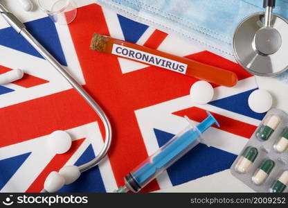 Coronavirus, nCoV concept. Top view protective breathing mask, stethoscope, syringe, pills on the flag of great Britain. A new outbreak of the Chinese coronavirus. Coronavirus, nCoV concept. Top view protective breathing mask, stethoscope, syringe, pills on the flag of great Britain.