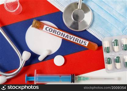 Coronavirus, nCoV concept. Top view protective breathing mask, stethoscope, syringe, tablets on the flag of Laos. A new outbreak of the Chinese coronavirus. Coronavirus, nCoV concept. Top view protective breathing mask, stethoscope, syringe, tablets on the flag of Laos.