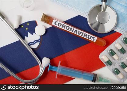 Coronavirus, nCoV concept. Top view protective breathing mask, stethoscope, syringe, tablets on the flag of Slovenia. A new outbreak of the Chinese coronavirus. Coronavirus, nCoV concept. Top view protective breathing mask, stethoscope, syringe, tablets on the flag of Slovenia.