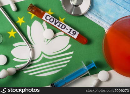 Coronavirus, the concept COVid-19. Top view of a protective breathing mask, stethoscope, syringe, pills on the flag of Macau. A new outbreak of the Chinese coronavirus. Coronavirus, the concept COVid-19. Top view of a protective breathing mask, stethoscope, syringe, pills on the flag of Macau.