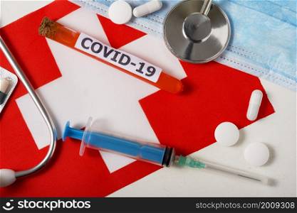 Coronavirus, the concept COVid-19. Top view protective breathing mask, stethoscope, syringe, pills on the flag of Switzerland. A new outbreak of the Chinese coronavirus. Coronavirus, the concept COVid-19. Top view protective breathing mask, stethoscope, syringe, pills on the flag of Switzerland.