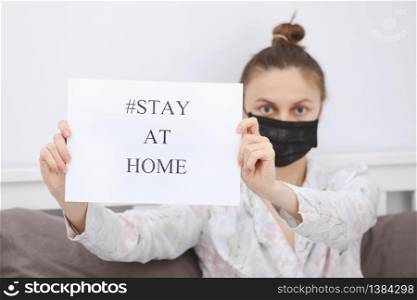 Coronavirus. Young woman in protection mask holding paper with Stay Home in her house. isolated to prevent infection of pandemic, epidemic Covid-19. Stop virus Quarantine at home. selective focus.. Coronavirus. Young woman in protection mask holding paper with Stay Home in her house. isolated to prevent infection of pandemic, epidemic Covid-19. Stop virus Quarantine at home. selective focus