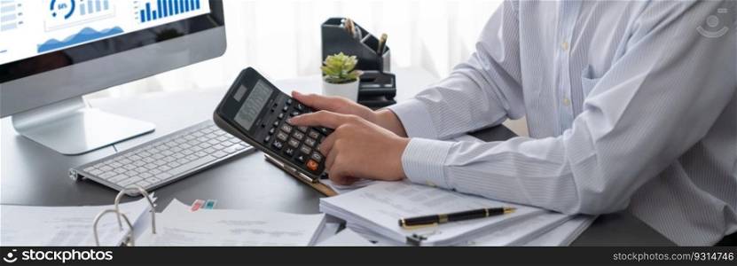 Corporate auditor calculating budget with calculator on his office desk. Dedicated accountant professional of accounting business company analyzing financial document to forecast income. Insight. Corporate auditor calculating budget with calculator on his office desk. Insight