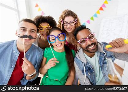 corporate, celebration and holidays concept - happy friends or team with party accessories having fun at office. happy friends or team having fun at office party