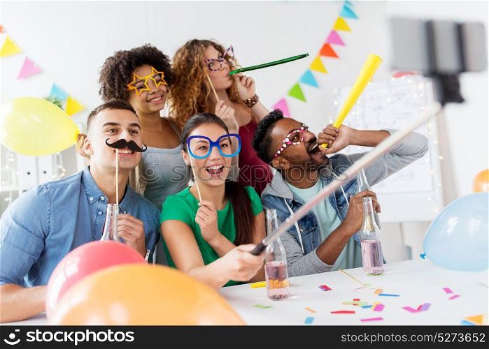 corporate, celebration and holidays concept - happy friends or team with party accessories taking selfie at office. happy team taking selfie at office party