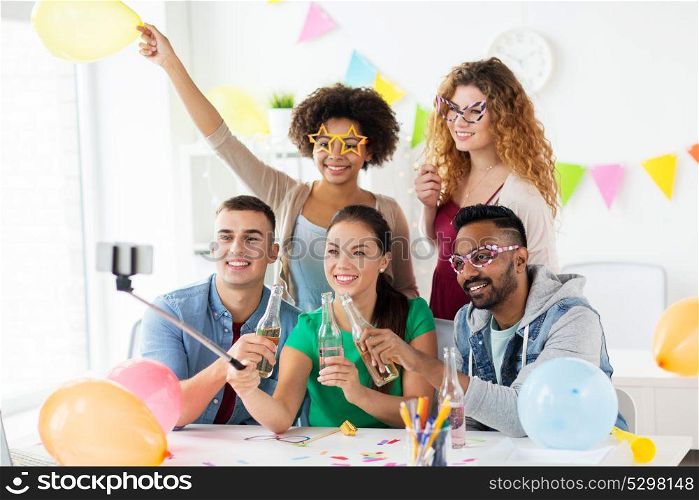corporate, celebration and holidays concept - happy friends or team with party accessories taking selfie at office. happy team taking selfie at office party