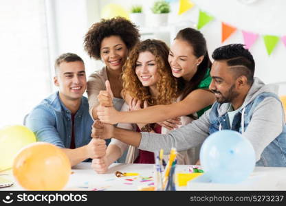 corporate, celebration and holidays concept - happy team with confetti having fun at office birthday party and showing thumbs up. happy team at office party showing thumbs up