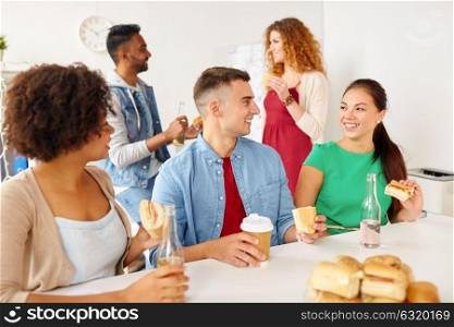 corporate, celebration and people concept - happy friends or team eating sandwiches with coffee and non-alcoholic drinks at office. happy friends or team eating at office