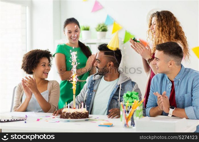 corporate, celebration and people concept - happy team with firework on birthday cake and non-alcoholic drinks greeting colleague at office party. team greeting colleague at office birthday party