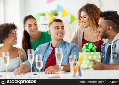 corporate, celebration and people concept - happy team with gifts and champagne glasses greeting colleague at office birthday party. team greeting colleague at office birthday party