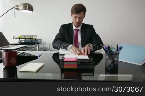 Corporate manager in modern office takes a break and prepares a paper airplane. The bored man thinks of his vacations and leans back on his chair with upset expression. Medium shot