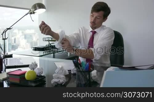 Corporate manager in modern office tries to write a job letter. The man is frustrated and keeps on screwing up paper. He feels anxious and rolls up his shirt sleeves. Medium shot