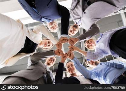 corporate, people and teamwork concept - happy business team making fist bump at office from below. happy business people making fist bump at office