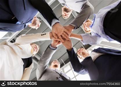 corporate, people and teamwork concept - happy business team stacking hands at office from below. happy business people stacking hands