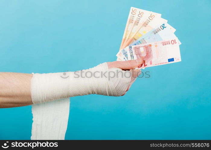 Corruption in healthcare industry. Part body male bandaged hand with money and long white bandage on blue.. Male bandaged hand with money.