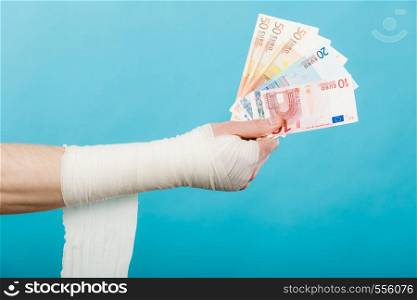 Corruption in healthcare industry. Part body male bandaged hand with money and long white bandage on blue.. Male bandaged hand with money.