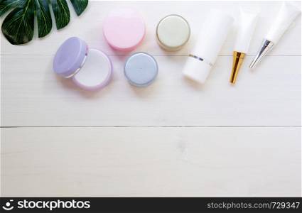 cosmetic and skin care product and green leaves on white wood table, beauty with treatment cream and moisturizing on wooden desk, health and wellness concept, top view.