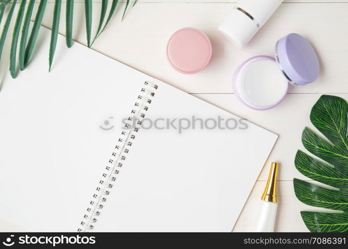 cosmetic and skin care product and notebook and leaves on table, beauty with treatment cream and moisturizing and notepad copy space on wooden desk, health and wellness concept, top view.